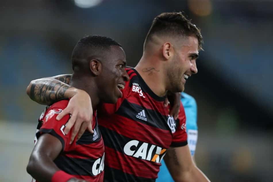 Vinicius Junior é abraçado por Felipe Vizeu; os dois estão sorrindo com a camisa do Flamengo em 2018