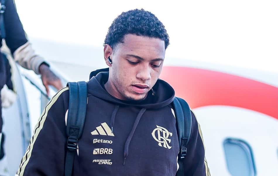 Daniel Sales descendo do avião com fone no ouvido e moletom marrom