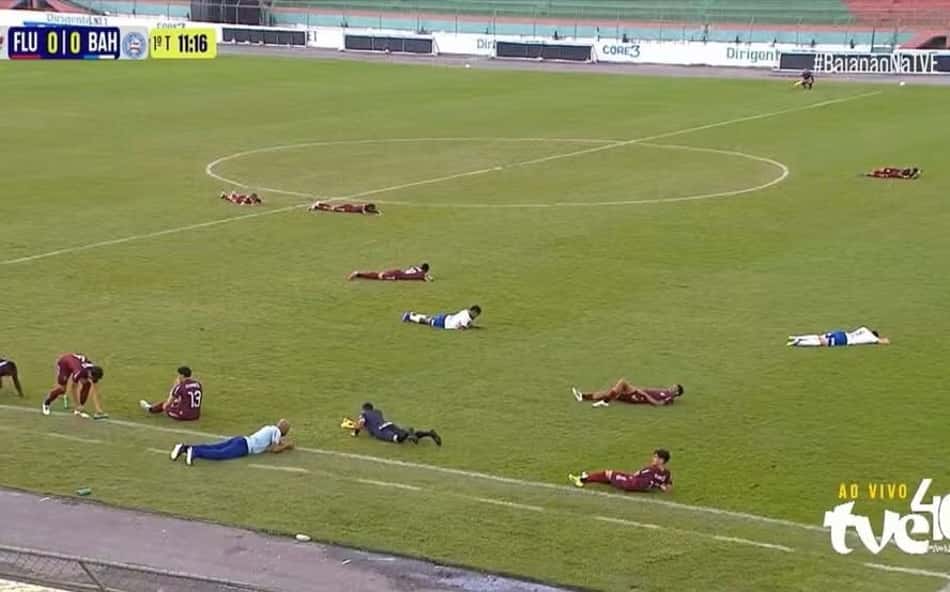 Jogadores, comissão técnica e árbitro deitados no chão do gramado