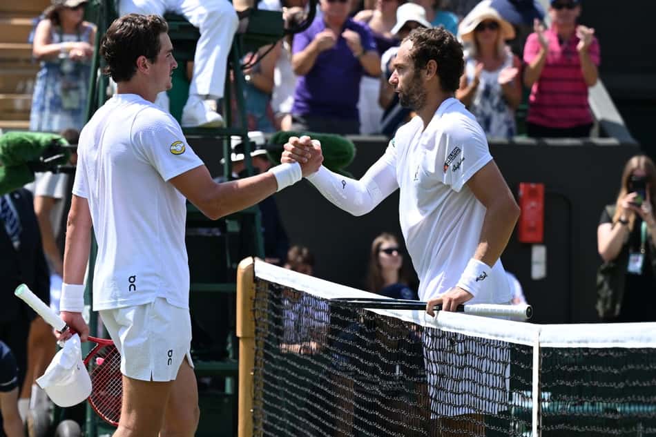 João Fonseca e Roman Safiullin, ambos vestidos de conjuntos brancos, se cumprimentam na rede do All England Club, em Londres, após se enfrentarem em Wimbledon