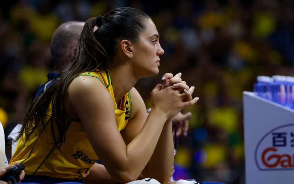Sentada, Julia Kudiess, com as mãos juntas, observa o jogo do Brasil do banco da comissão técnica