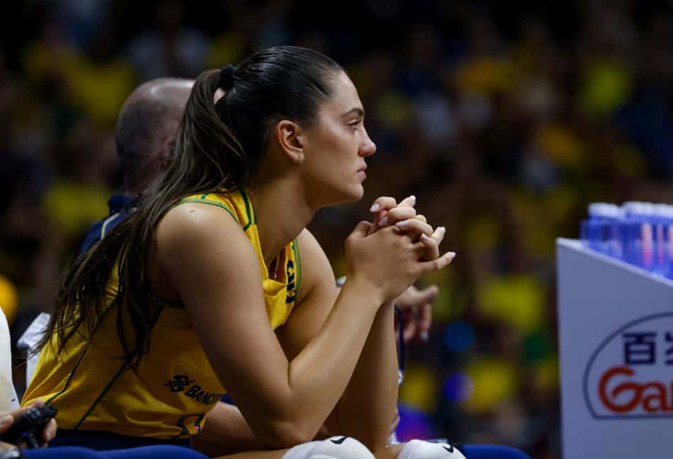 Sentada, Julia Kudiess, com as mãos juntas, observa o jogo do Brasil do banco da comissão técnica