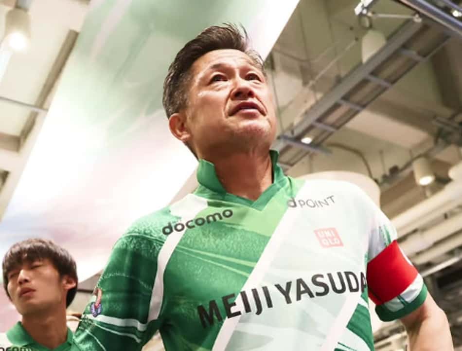 Kazu Miura olhando para cima com uniforme verde com uma faixa branca
