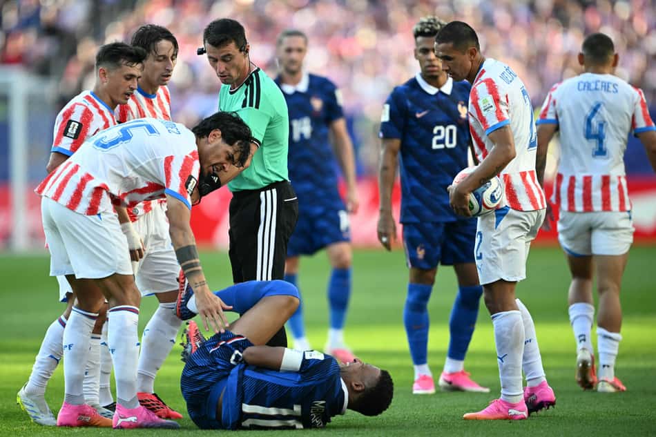 Mbappé caído no gramado após sofrer falta ao lado de Gustavo Gomez em França x Paraguai
