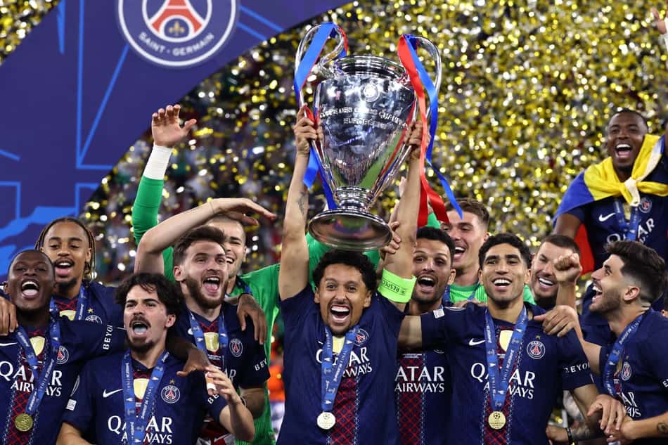 Marquinhos levanta a taça da Champions League, cercado por jogadores do PSG.