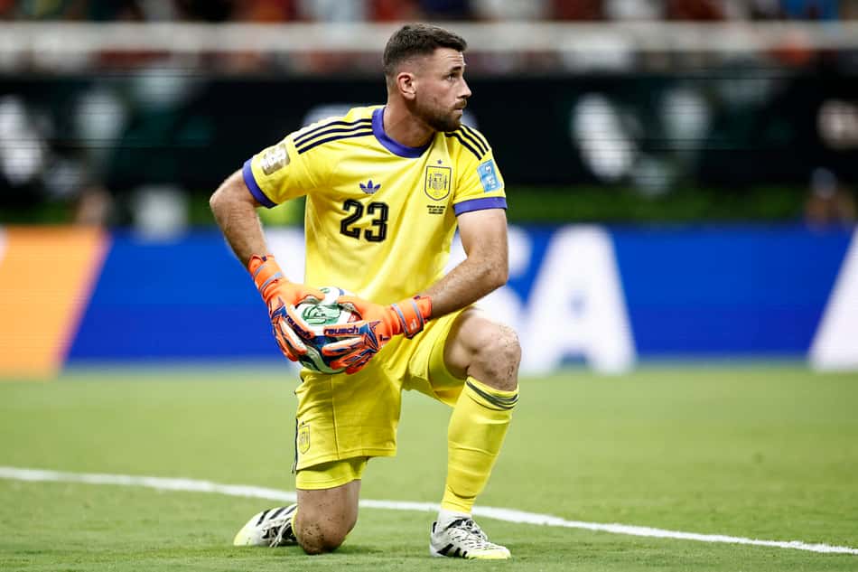 Unai Simon, goleiro da Espanha na Copa, com o joelho no gramado, segurando a bola para repor em jogo para a Espanha. 