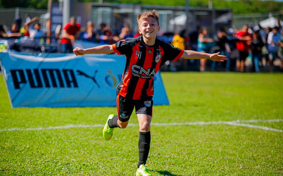 Participante do projeto IberCup correndo de braços abertos com uniforme vermelho e preto