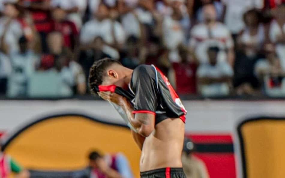 Jogador do Bahia vibrando e jogador do Vitória de cabeça baixa ao fundo