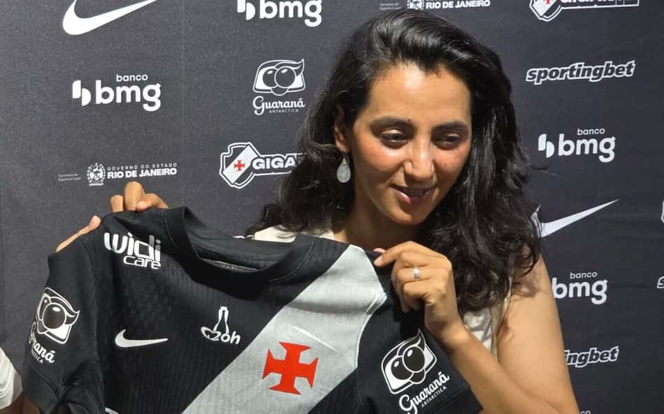 Khalida Popal na frente de um background com marcas parceiras do Vasco segurando uma camisa do clube