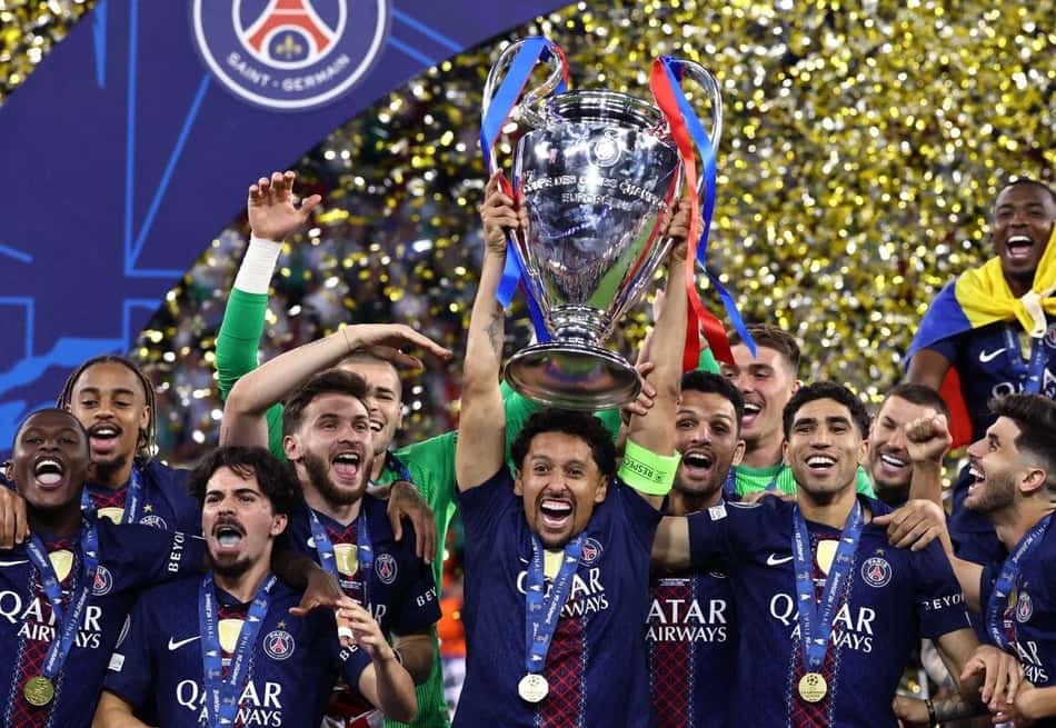 Marquinhos levanta a taça da Champions League, cercado por jogadores do PSG.