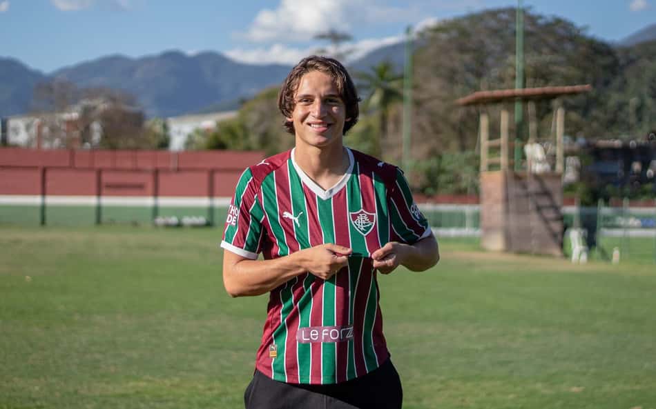 Ruan posa com camisa do Fluminense e segura o escudo no CT