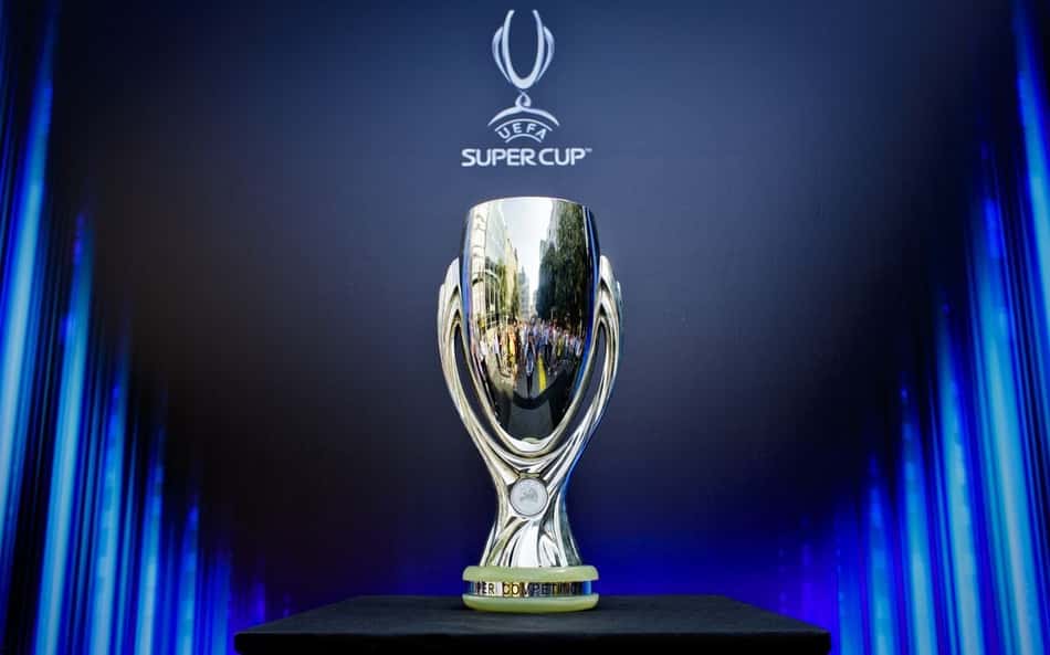 Taça da Supercopa em cima de uma mesa com uma tela atrás de anuncio do torneio com a logo oficial
