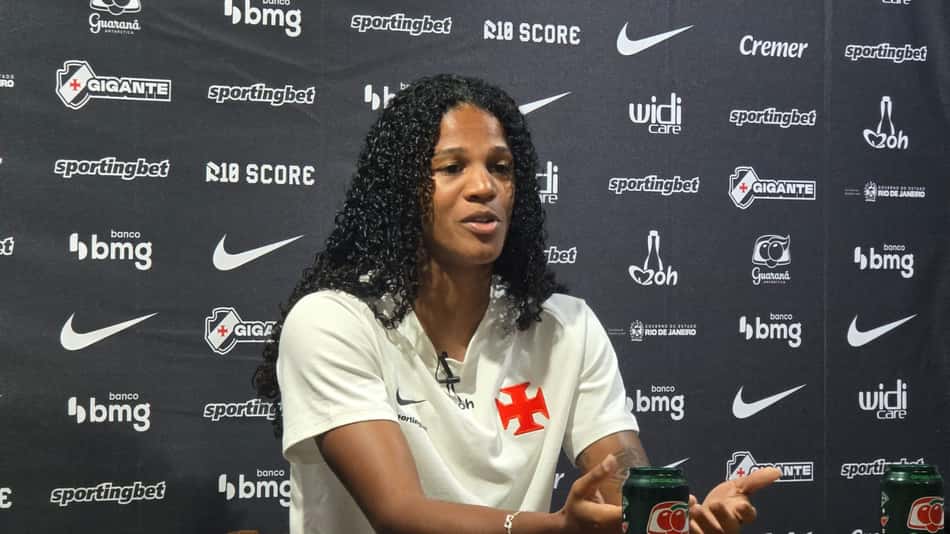 Vilama com camisa do VAsco atrás na imagem um Backdrop com patrocinadores do clube