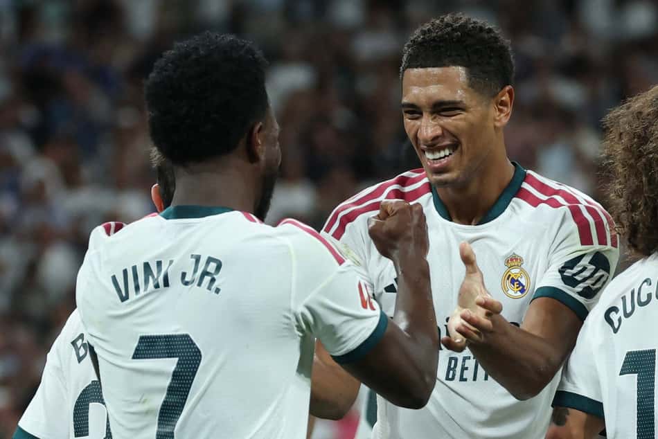 O atacante brasileiro do Real Madrid, número 7, Vinicius Junior (à esquerda), comemora o terceiro gol de sua equipe com o meio-campista inglês do Real Madrid, número 5, Jude Bellingham, durante a partida do Campeonato Espanhol entre Real Madrid CF e Real Sociedad, no Estádio Santiago Bernabéu, em Madri, em 26 de agosto de 2026
