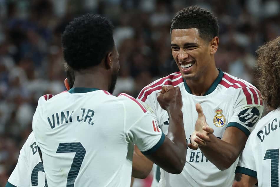 O atacante brasileiro do Real Madrid, número 7, Vinicius Junior (à esquerda), comemora o terceiro gol de sua equipe com o meio-campista inglês do Real Madrid, número 5, Jude Bellingham, durante a partida do Campeonato Espanhol entre Real Madrid CF e Real Sociedad, no Estádio Santiago Bernabéu, em Madri, em 26 de agosto de 2026