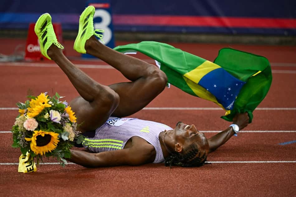 Alison dos Santos segura a bandeira do Brasil enquanto comemora o recorde mundial nos 400m com barreiras