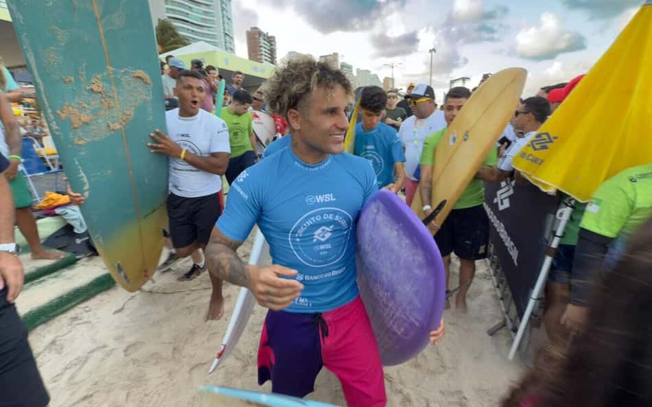 Na areia da praia de Saquarema, Ítalo Ferreira segura prancha com o braço esquerdo e é cercado por fãs durante etapa da WSL 2026