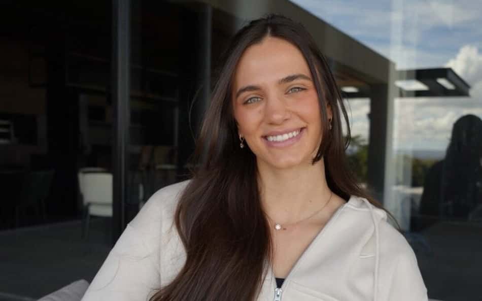 Julia Kudiess sorri para a câmera, sentada e usando um casaco