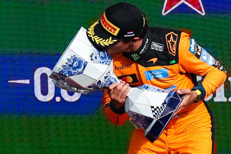 De boné e com o macacão da McLaren, Lando Norris inclina o corpo e beija o troféu do Grande Prêmio da Holanda de Fórmula 1 2026