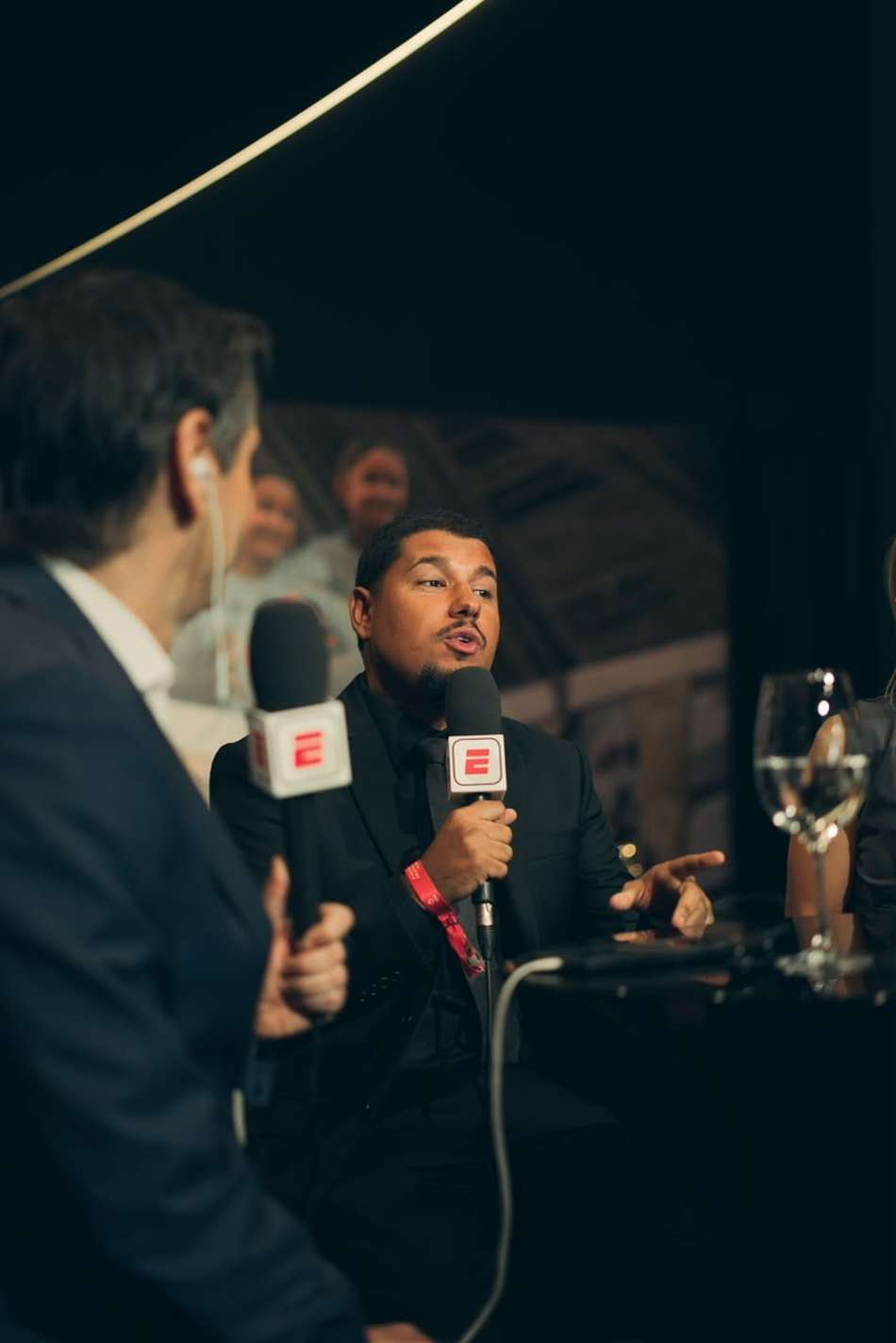 De terno, Lucas Tylty segura microfone da ESPN durante debate em mesa