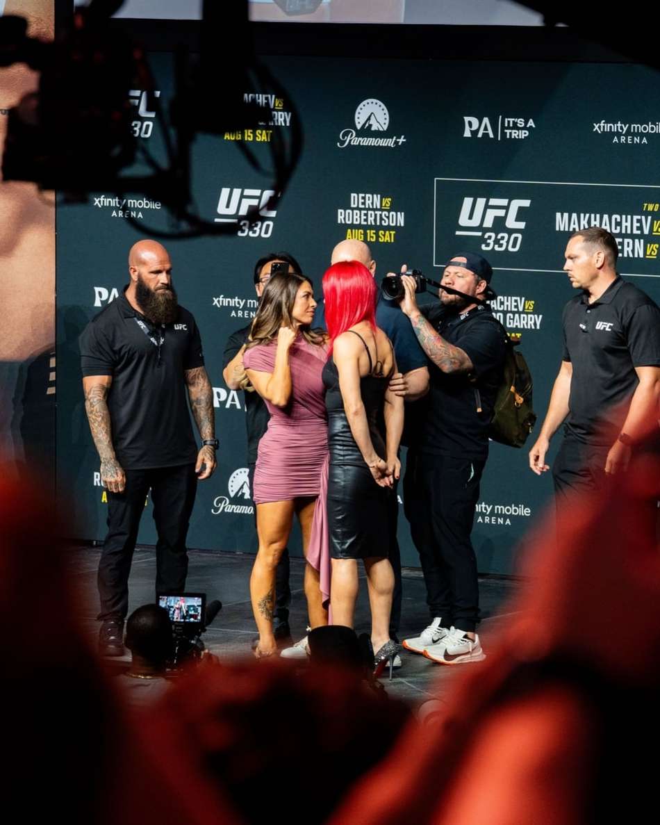 Cercadas por seguranças e representantes do UFC, Mackenzie Dern, à esquerda, e Gillian Robertson, à direita e de cabelo vermelho, se encaram durante pesagem cerimonial do UFC 330