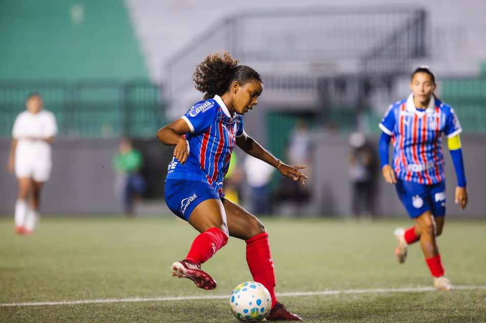Suelen com o uniforme azul e vermelho do Bahia com a bola em jogo