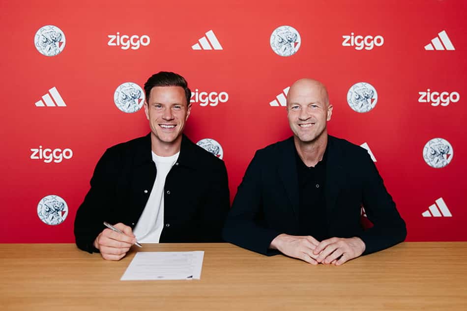 Ter Stegen de casaco preto e blusa branca com caneta na mão ao lado de Jordi Cruyff sentados à mesa