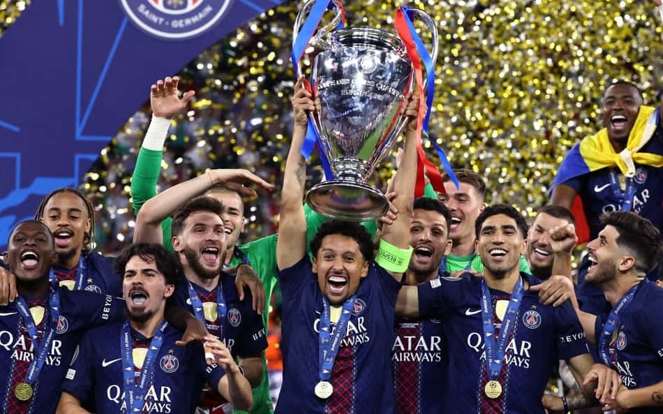 Marquinhos levanta a taça da Champions League, cercado por jogadores do PSG.