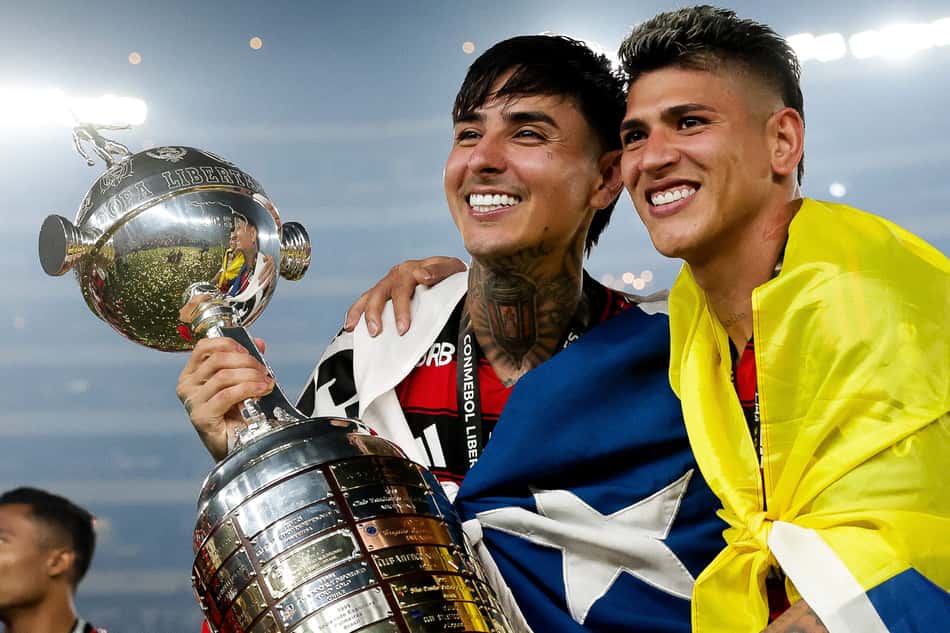 Pulgar, enrolado na bandeira do Chile, e Carrascal, enrolado na bandeira da Colômbia, levantam troféu da Libertadores de 2025 conquistado pelo Flamengo