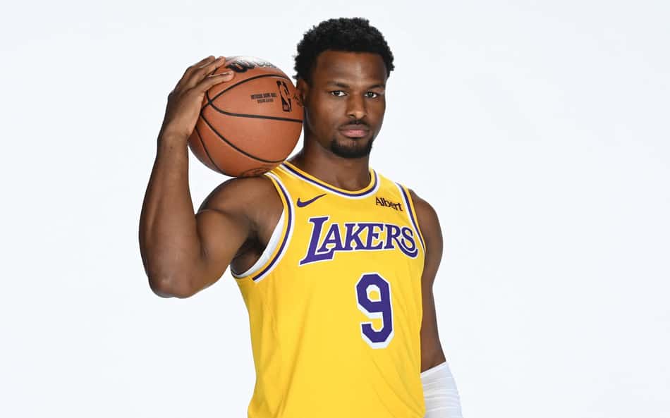 Bronny James segura a bola com a mão direita e a apoia no ombro em sessão de fotos do Los Angeles Lakers