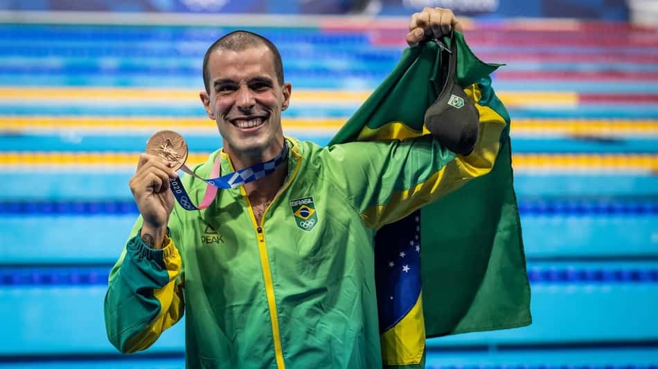 O nadador Bruno Fratus segura a bandeira do Brasil e mostra a medalha de bronze nos Jogos Olímpicos de Tóquio