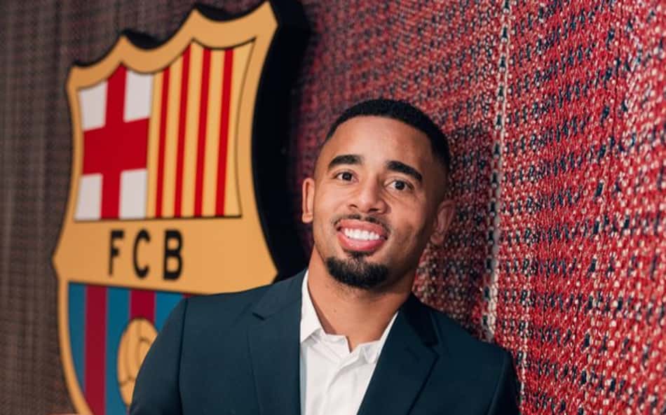 Com escudo do Barcelona atrás, Gabriel Jesus sorri de terno