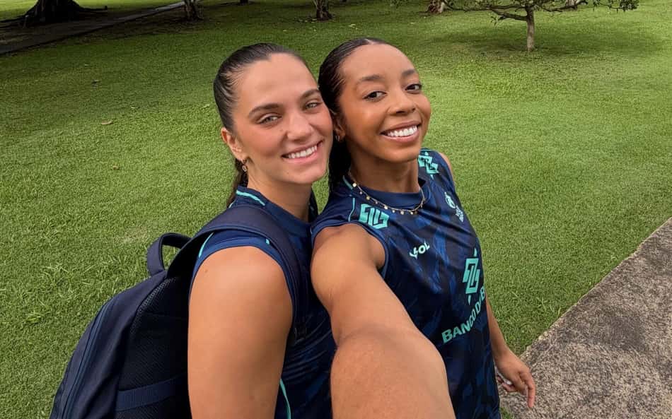 A oposta Kisy, à direita, segura o celular com a mão esquerda e tira selfie encostada na central Julia Kudiess, à esquerda