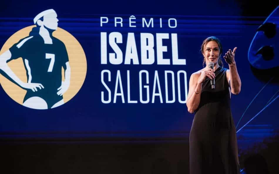 Ex-atleta de vôlei de praia, Maria Clara Salgado discursa em pé, em frente ao painel do Prêmio Isabel Salgado