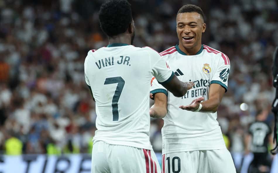 O atacante brasileiro do Real Madrid, número 7, Vinicius Junior (à esquerda), comemora o terceiro gol de sua equipe com o atacante francês do Real Madrid, número 10, Kylian Mbappé, durante a partida do Campeonato Espanhol entre Real Madrid CF e Real Sociedad, no Estádio Santiago Bernabéu, em Madri, em 26 de agosto de 2026