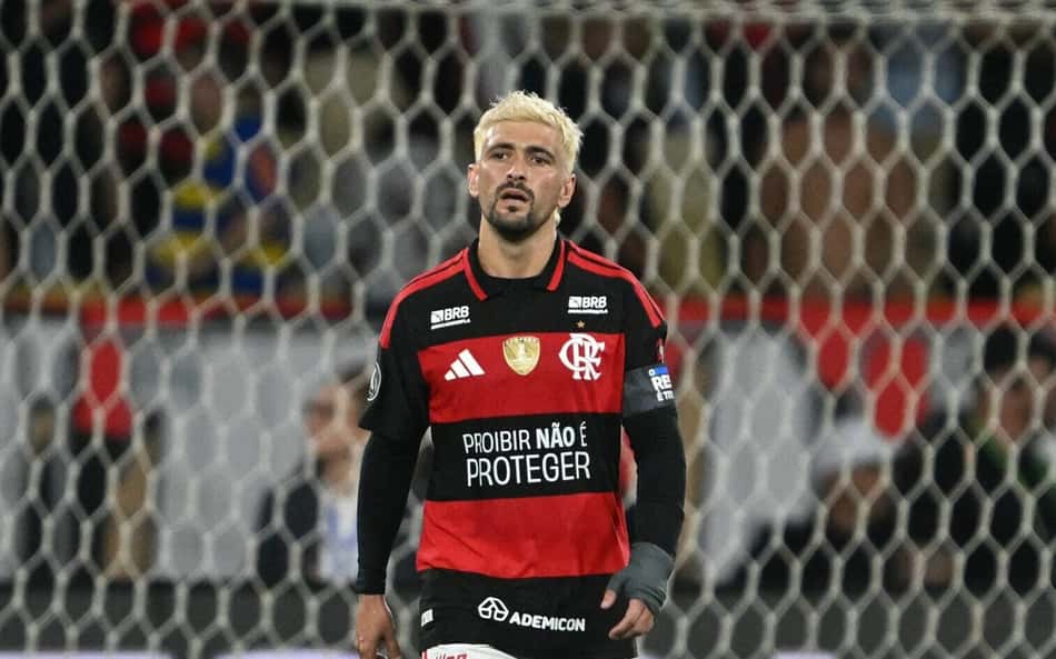 Jogador do Flamengo, camisa preta e vermelha com o número 10, em campo durante a partida, torcedores ao fundo.