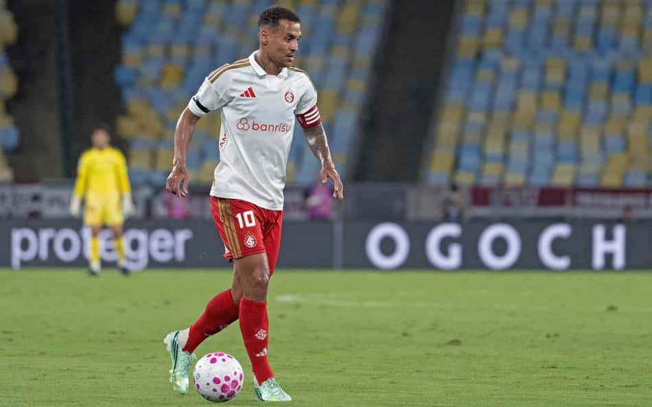 Alan Patrick, jogador do Internacional, com camisa branca e shorts vermelhos, controlando a bola em campo.