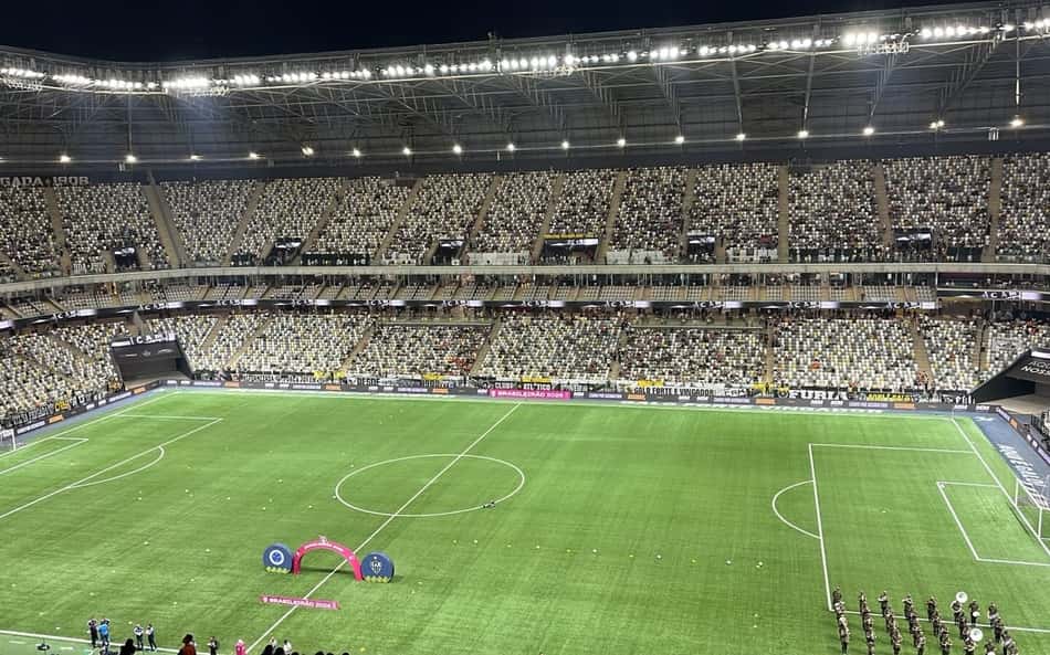 Arena MRV TR: estádio de futebol com arquibancadas cheias e gramado, arco rosa ao centro para cerimônia.