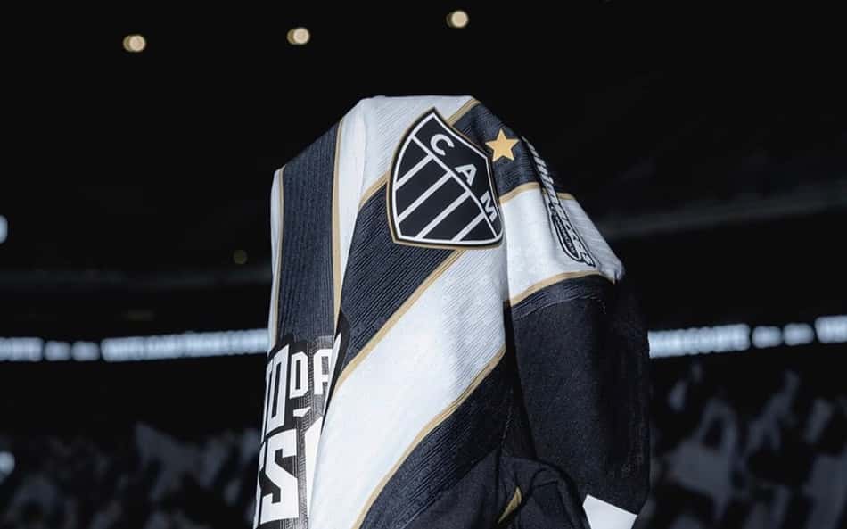 Camisa do Atlético Mineiro (CAM) para o clássico contra Cruzeiro, com listras pretas e brancas e detalhes dourados.