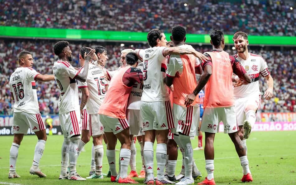 Jogadores do Flamengo se abraçam em comemoração no gramado, torcida lotada ao fundo.