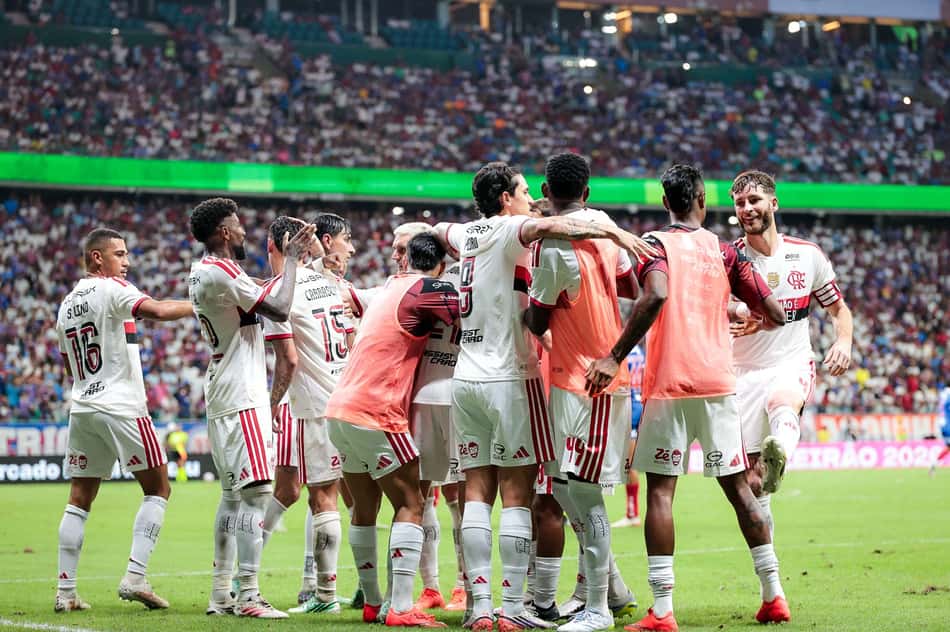 Jogadores do Flamengo se abraçam em comemoração no gramado, torcida lotada ao fundo.