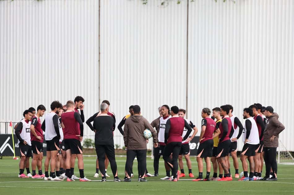 Grupo de jogadores do Corinthians em treino, ouvindo instruções de treinadores no campo