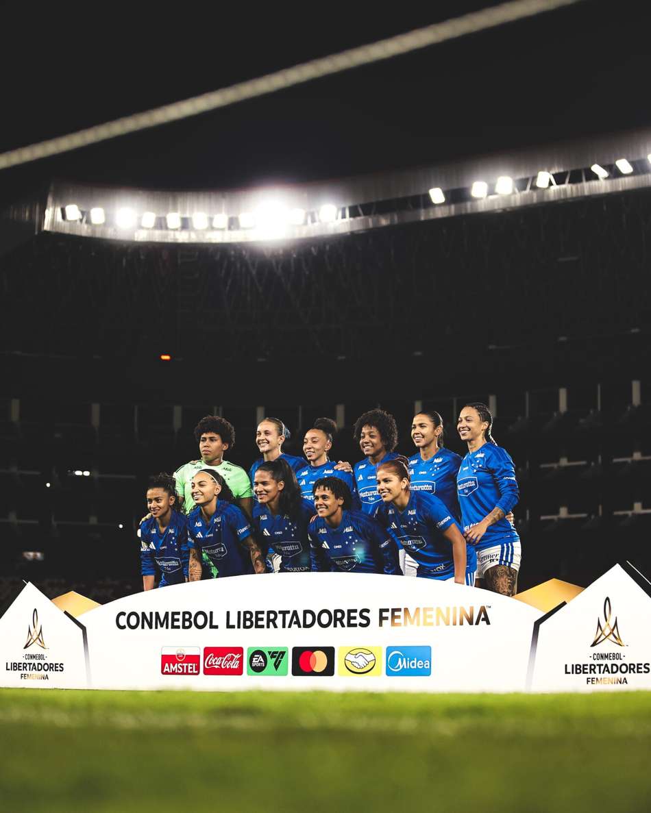 Equipe feminina do Cruzeiro posa na CONMEBOL Libertadores Femenina, em frente ao banner oficial.
