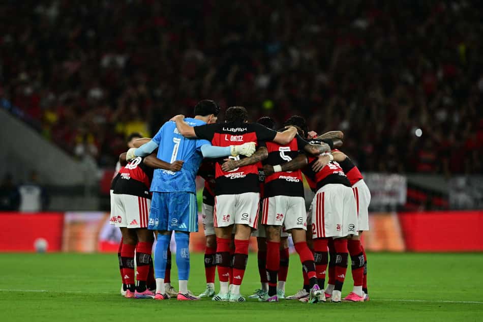 Elenco do Flamengo em abraço coletivo no gramado, goleiro azul ao centro.