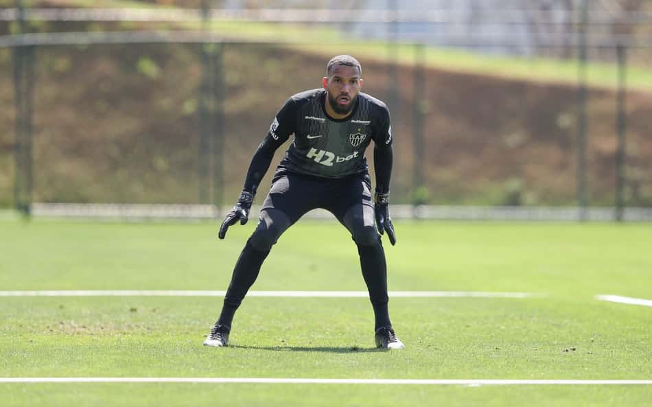 Éverson, goleiro, em treino de futebol, com luvas pretas, em posição defensiva no campo verde.