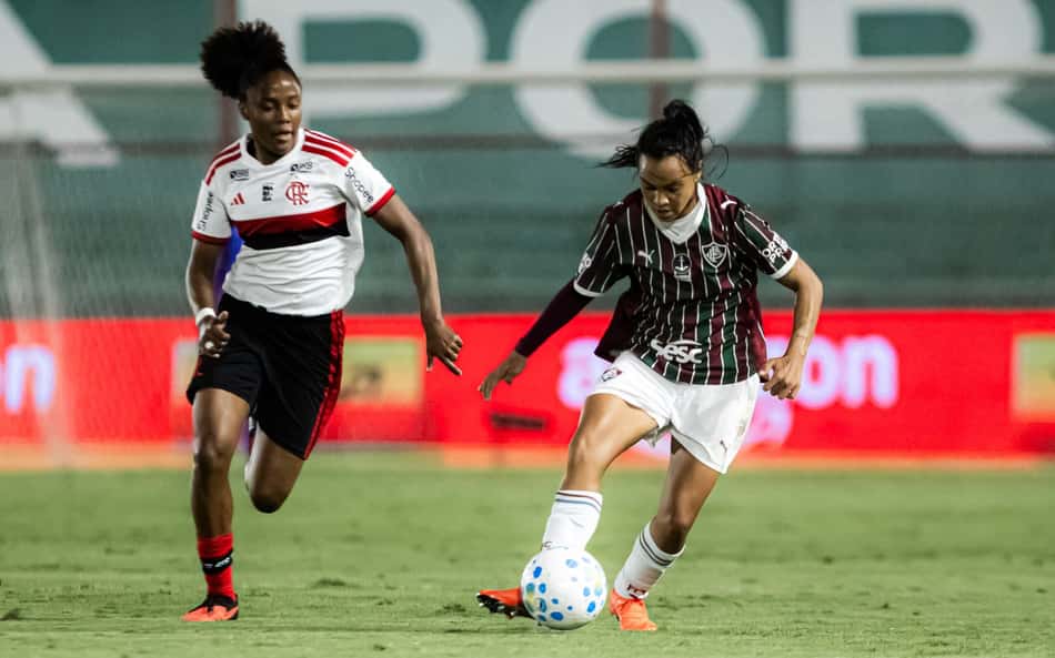 Duas jogadoras de futebol feminino, Flamengo x Fluminense, disputando a bola em campo.