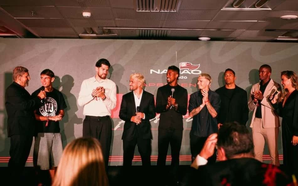 Grupo no palco durante leilão, alguns segurando microfones; fundo com logotipo e público ao redor.