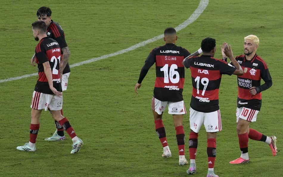 Flamengo comemorando em campo, com camisas pretas e vermelhas, números 16, 19 e 10.