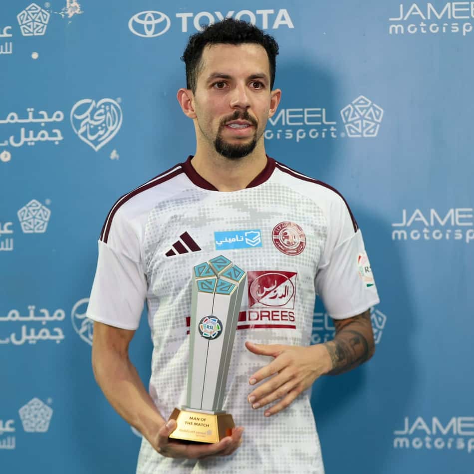 Flavio segura o troféu Man of the Match, vestindo uniforme branco, diante de fundo azul com logos.