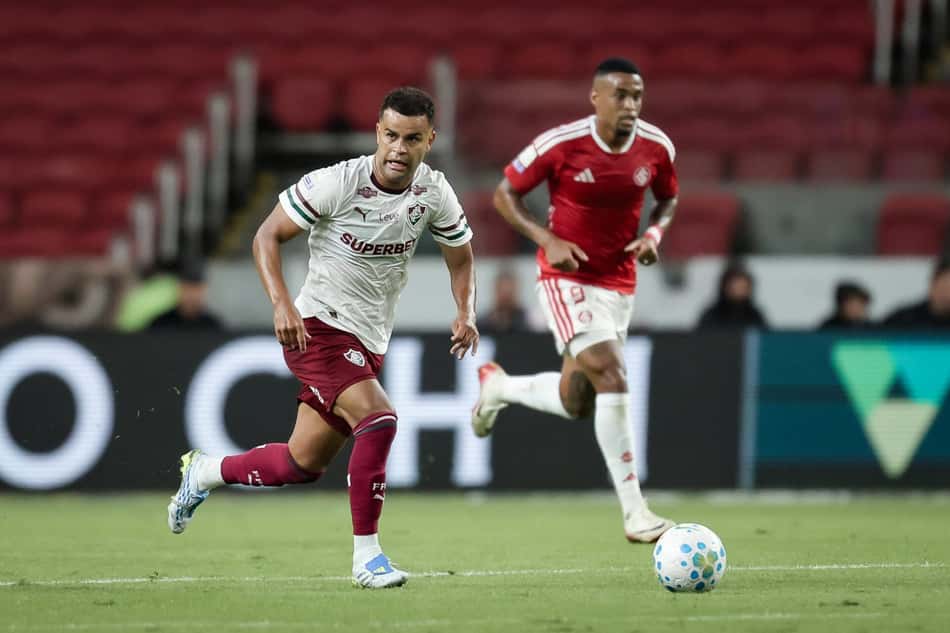 Jogador do Fluminense com camisa branca avança com a bola, perseguido pelo Internacional em campo.